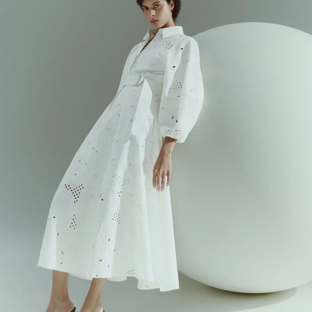 White Akris broderie anglaise dress with full sleeves photographed against a pale form White Akris broderie anglaise dress with full sleeves photographed against a pale form