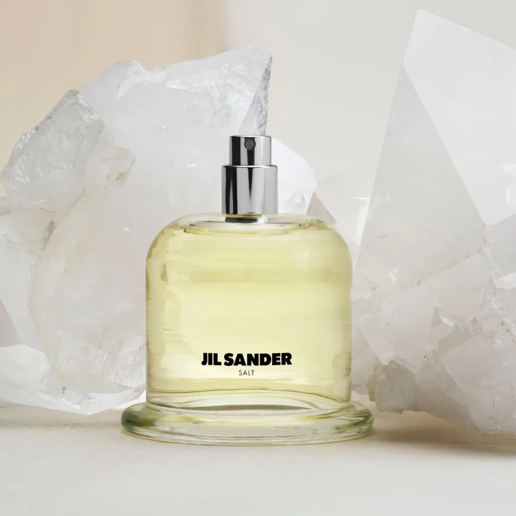Jil Sander fragrance bottle photographed beside raw quartz crystal in a pale still life Jil Sander fragrance bottle photographed beside raw quartz crystal in a pale still life