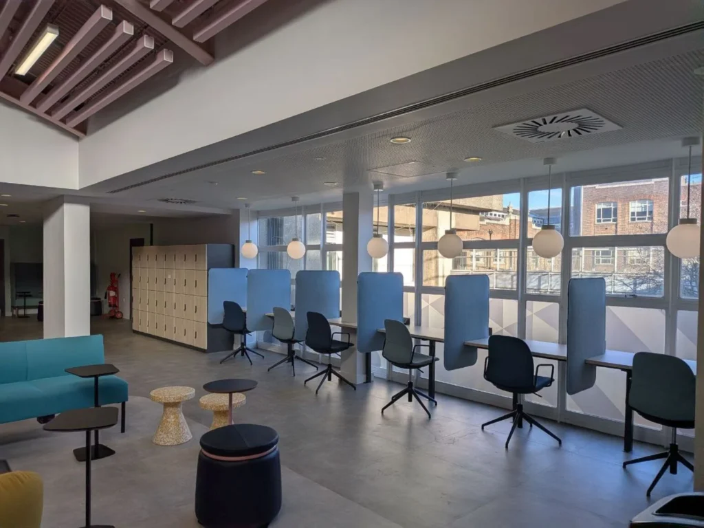 Making Every Square Foot Count: Smarter Office Design in Mayfair Bright open-plan London office with blue upholstered focus booths, desks along a wall of windows and lounge seating