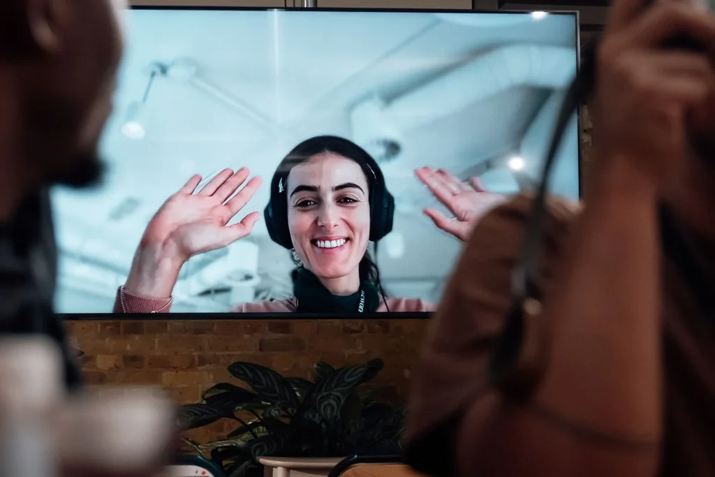 Making Every Square Foot Count: Smarter Office Design in Mayfair Smiling woman in headphones waving from a large video-call screen in a shared office, with colleagues in the foreground