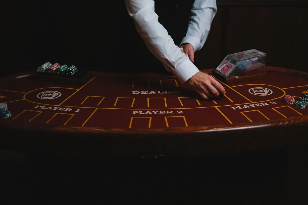 Croupier's hands dealing cards on a dark wooden gaming table marked with player positions