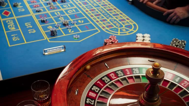 Roulette wheel beside a betting table with stacked chips and a glass of whisky